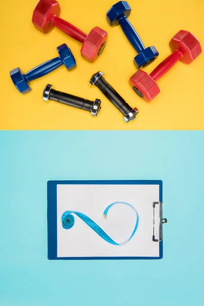 Sports dumbbells and clipboard isolated on yellow and blue — Stock Photo