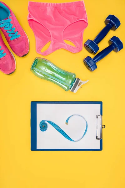 Sports equipment with shoes, dumbbells, sports top and clipboard isolated on yellow — Stock Photo