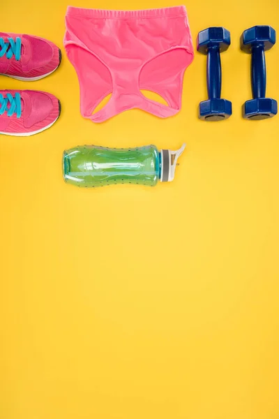 Sports equipment with shoes, dumbbells, sports top and water bottle isolated on yellow — Stock Photo