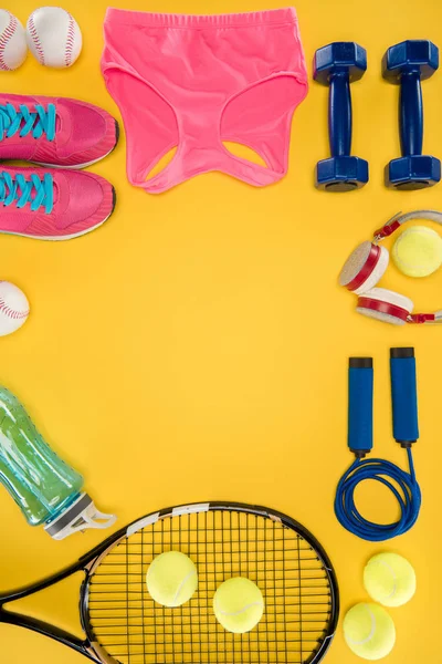 Equipamiento deportivo con zapatos, mancuernas, top deportivo y auriculares aislados en amarillo - foto de stock