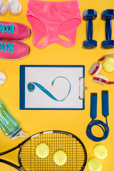 Equipamiento deportivo con zapatos, mancuernas, top deportivo y portapapeles aislados en amarillo - foto de stock