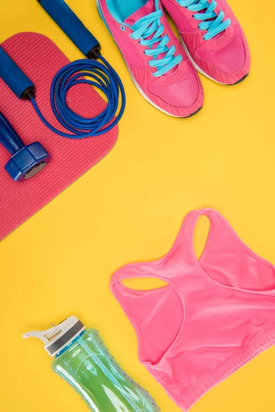 Sports equipment with shoes, dumbbell, sports top and skipping rope isolated on yellow — Stock Photo