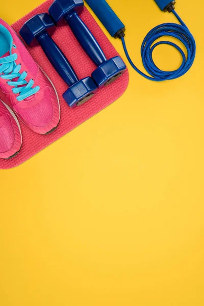 Equipamento desportivo com sapatos, halteres e pular corda isolada em amarelo — Fotografia de Stock