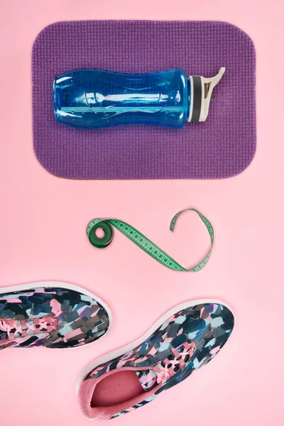 Sapatos esportivos e garrafa de água com fita métrica isolada em rosa — Fotografia de Stock