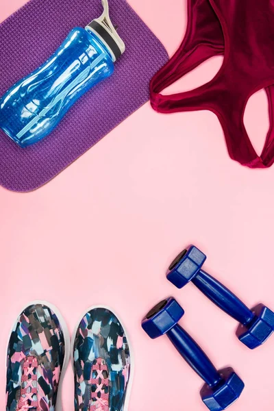 Спортивный инвентарь с обуви, гантели, спортивный топ и бутылка воды изолированы на розовый — стоковое фото