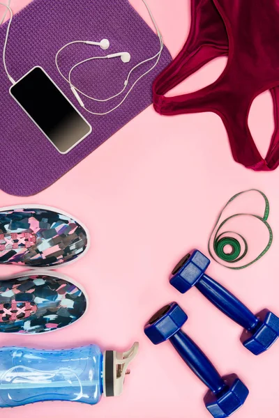 Equipamiento deportivo con zapatos, mancuernas, top deportivo y smartphone aislados en rosa - foto de stock
