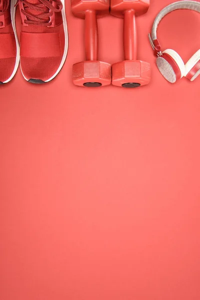 Equipamiento deportivo con zapatos, mancuernas y auriculares aislados en rojo - foto de stock