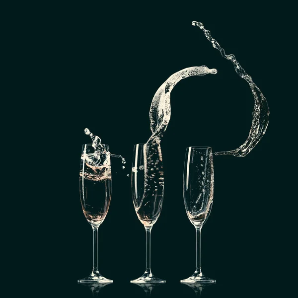 Tre bicchieri con spruzzi di champagne su nero — Foto stock