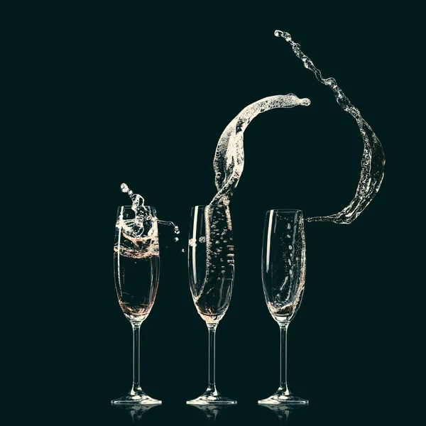 Three glasses with splashes of champagne on black — Stock Photo