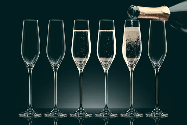 Pouring champagne from bottle into six transparent glasses on black — Stock Photo