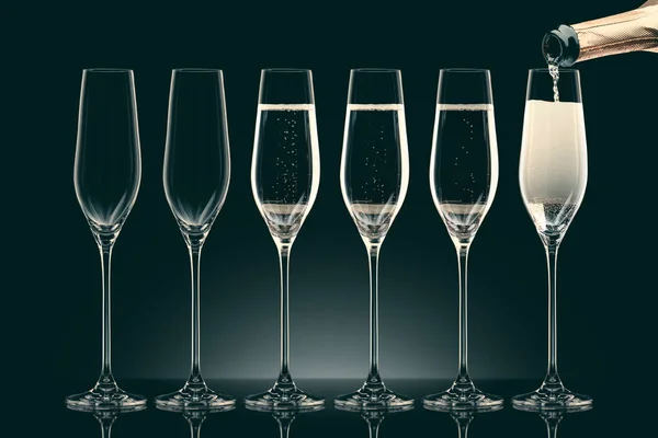 El champán que vierte de la botella en seis vasos transparentes sobre negro - foto de stock