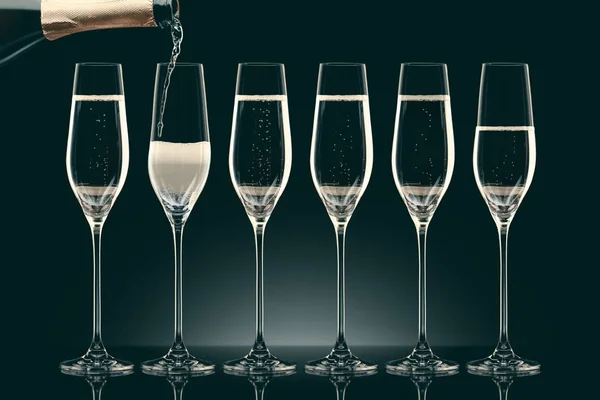El champán que vierte de la botella en seis vasos transparentes sobre negro - foto de stock