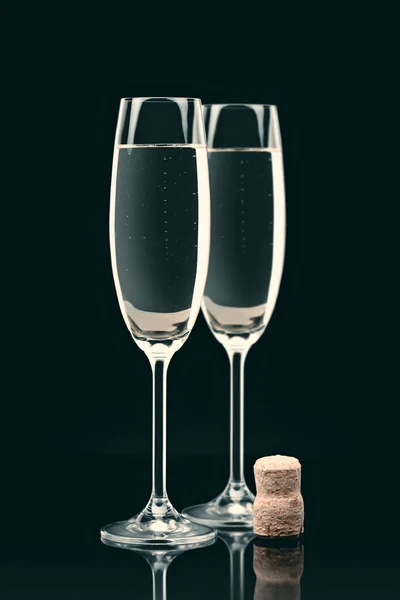Two transparent glasses with calm champagne and cork on table on black — Stock Photo