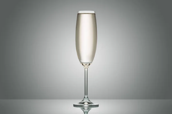 One transparent glass with calm champagne on grey — Stock Photo