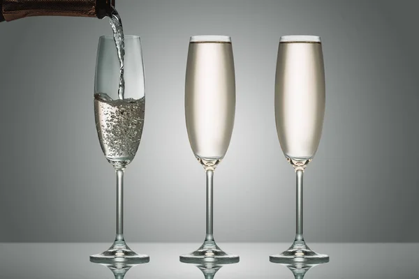 El champán que vierte de la botella en tres vasos sobre gris - foto de stock