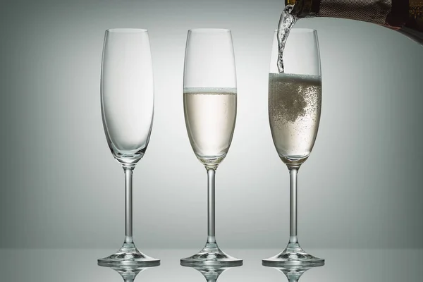 El champán que vierte de la botella en tres vasos sobre blanco - foto de stock
