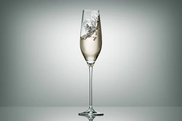 Splashing champagne in transparent glass on white — Stock Photo