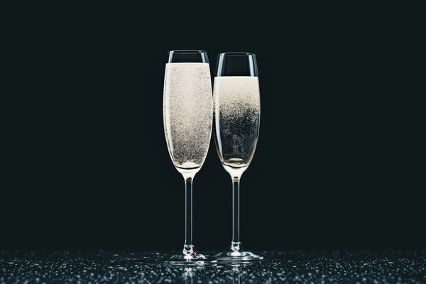 Two glasses with champagne with drops on table on black — Stock Photo