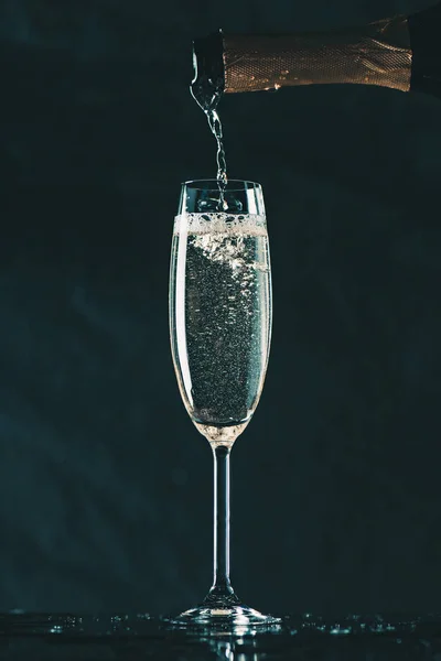Pouring champagne from bottle into glass on black — Stock Photo