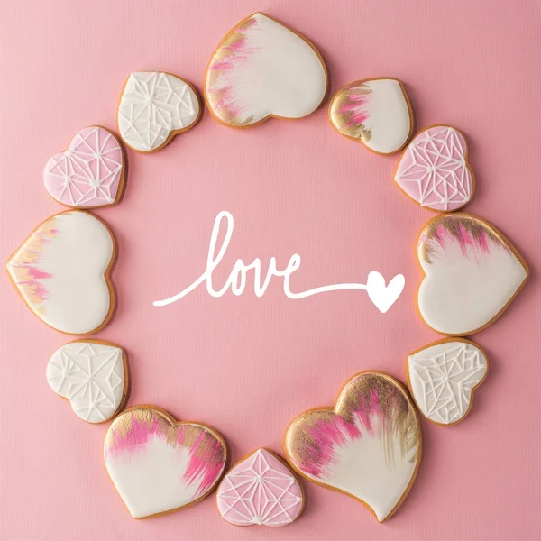 Tendido plano con disposición de galletas esmaltadas en forma de corazón aisladas en la superficie de color rosa - foto de stock