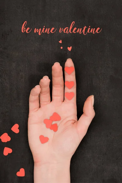 Partial view of female hand and red heart shaped confetti on dark background, st valentines day concept — Stock Photo