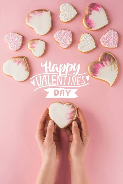 Partial view of woman holding glazed cookie in hands isolated on pink, st valentines day concept — Stock Photo