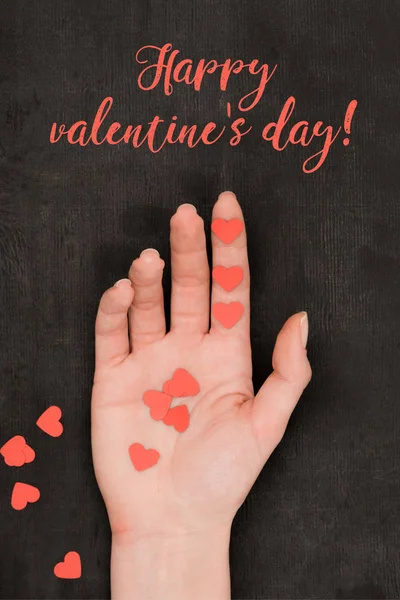 Partial view of female hand and red heart shaped confetti on dark background, st valentines day concept — Stock Photo