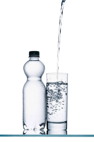 Натюрморт з пластиковою пляшкою і водою, що вливається в скло ізольовано на білому — стокове фото