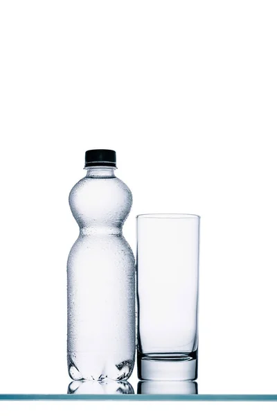 Full plastic bottle of water and empty glass isolated on white — Stock Photo