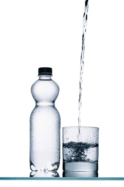 Wet plastic bottle and water pouring into glass isolated on white — Stock Photo