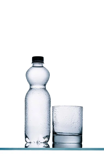 Wet full plastic bottle of water and empty glass isolated on white — Stock Photo