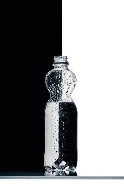 Plastikflasche mit Wasser auf halb schwarzem und weißem Hintergrund — Stockfoto