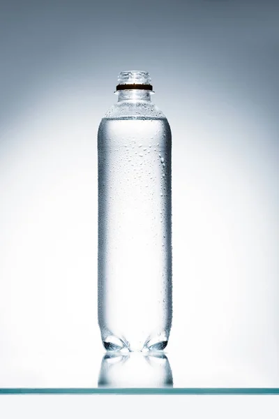 Plastikflasche voller Wasser auf reflektierender Oberfläche — Stockfoto