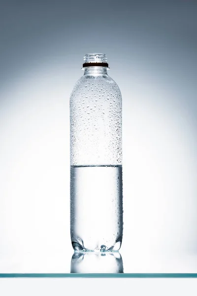 Demi pleine bouteille d'eau en plastique sur la surface réfléchissante — Photo de stock