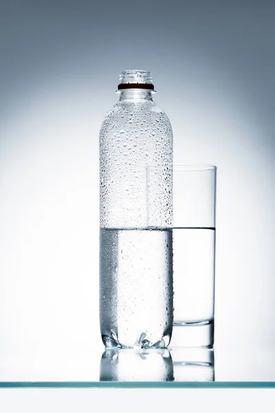 Botella de plástico y vidrio de agua en la superficie reflectante - foto de stock