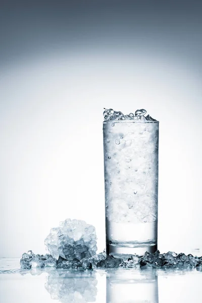 Glass of cold water with ice on reflective surface on white — Stock Photo