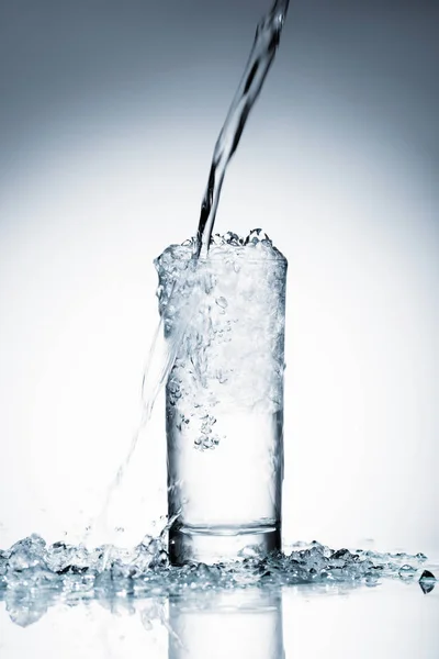 Plan rapproché de l'eau coulant dans le verre sur blanc — Photo de stock