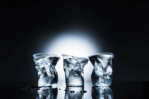 Vasos de plástico arrugado de agua en la oscuridad - foto de stock