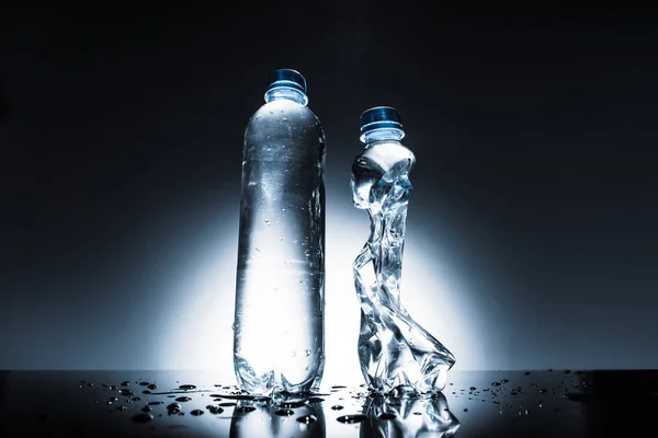 Botellas de agua intactas y arrugadas en la oscuridad - foto de stock