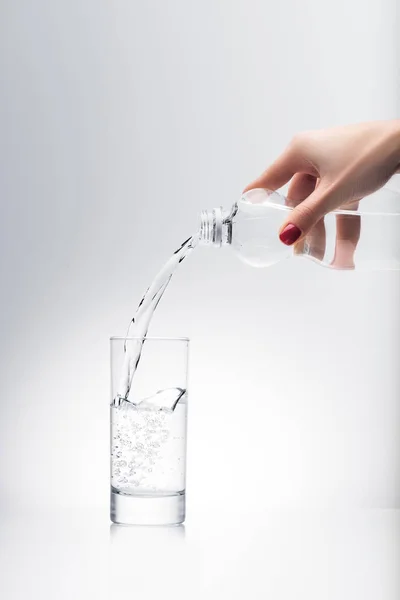 Tiro recortado de la mujer vertiendo agua en el vidrio de la botella de plástico - foto de stock
