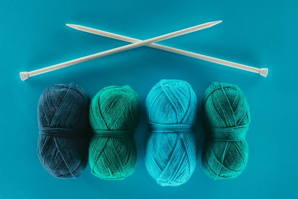 Draufsicht auf blaues und grünes Strickgarn mit Stricknadeln, isoliert auf blau — Stockfoto