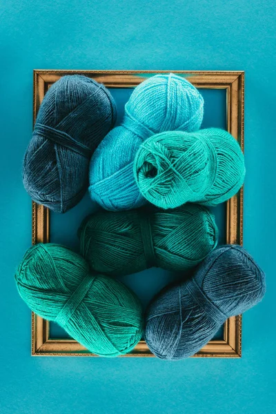 Vue de dessus des boules de tricot bleu et vert sur le cadre, isolées sur bleu — Photo de stock