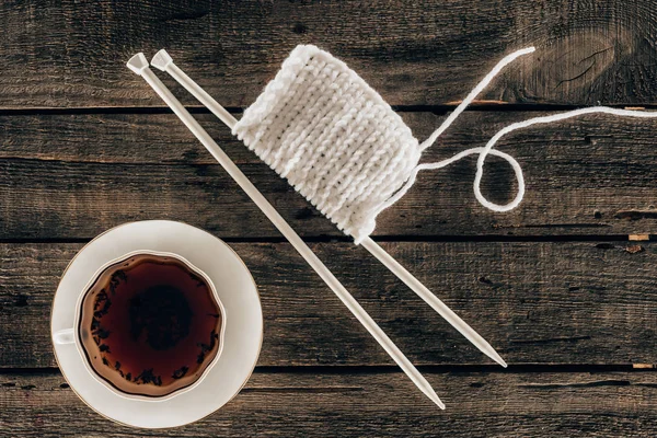 Top view of knitting needles with yarn and cup of tea on wooden background — Stock Photo