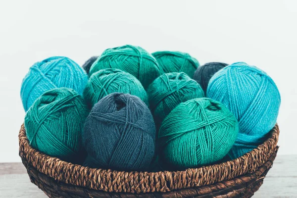 Blue and green knitting wool balls in wicker basket on white — Stock Photo