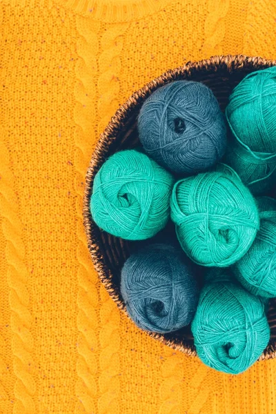 Top view of blue and green knitting yarn balls in wicker basket on yellow knit — Stock Photo