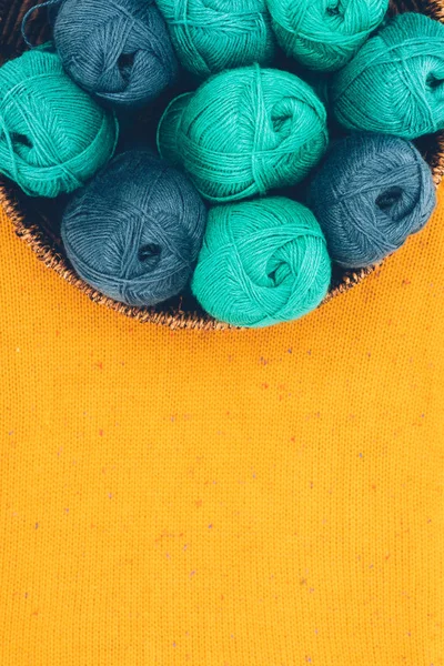 Vue de dessus des boules de laine tricotées bleues et vertes dans un panier en osier sur maille jaune — Photo de stock