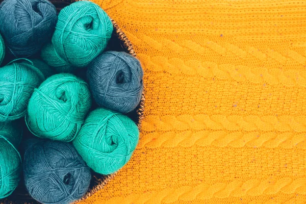 Draufsicht auf blaue und grüne Strickgarnbälle im Weidenkorb auf gelbem Strick — Stockfoto