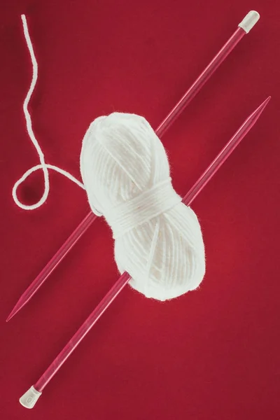 Vue de dessus de boule de fil blanc et aiguilles à tricoter, isolé sur rouge — Photo de stock