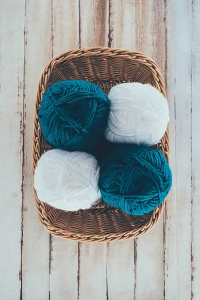 Top view of white and blue knitting wool balls in wicker basket on wooden background — Stock Photo