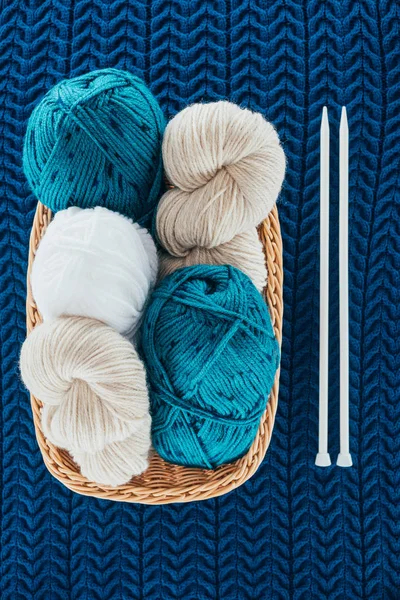 Top view of different knitting yarn balls in wicker basket with knitting needles on knit background — Stock Photo